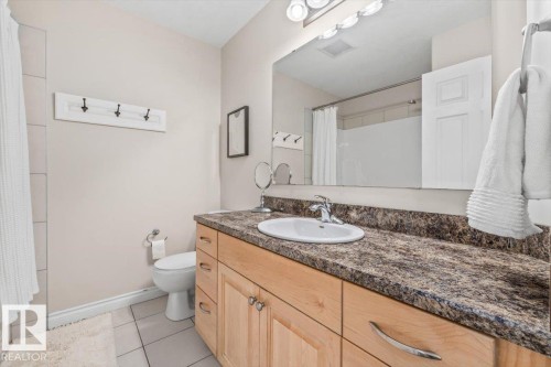This bathroom features a light wood vanity with a stone-look countertop, an integrated sink, and a large mirror with overhead lighting - 8737 83 Avenue, Edmonton, AB - Indoor Photo Showing Bathroom