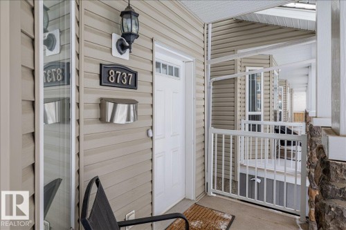 The property entrance features light-coloured siding, a white front door, and a wall-mounted light fixture - 8737 83 Avenue, Edmonton, AB - Outdoor With Exterior