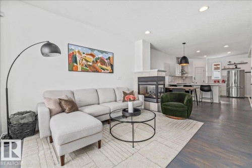 The living area features a fireplace with a tiled surround and an open layout leading to the kitchen, highlighted by recessed lighting and hardwood floors - 8737 83 Avenue, Edmonton, AB - Indoor Photo Showing Living Room