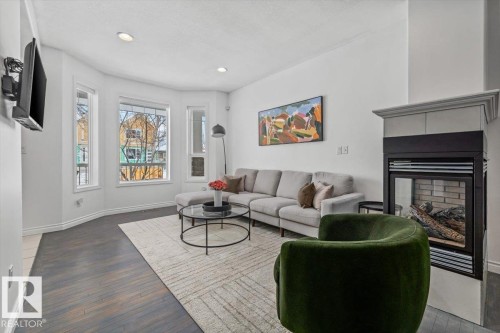 The living area features abundant natural light from multiple windows, dark hardwood flooring, and a fireplace - 8737 83 Avenue, Edmonton, AB - Indoor Photo Showing Living Room With Fireplace
