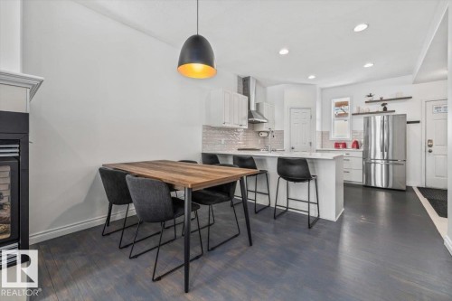 Open-concept living area featuring a fireplace with a white mantel, and a kitchen with white cabinetry and stainless steel appliances - 8737 83 Avenue, Edmonton, AB - Indoor