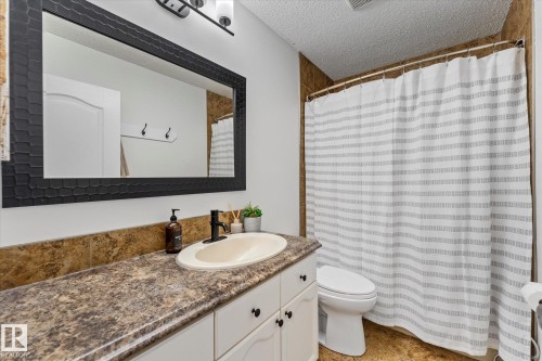 The bathroom features a vanity with a large mirror, a countertop with an integrated sink, and a shower with a striped curtain - 3908 44 Avenue, Stony Plain, AB - Indoor Photo Showing Bathroom