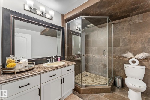 The bathroom features a spacious vanity with white cabinetry, a large mirror, and a glass-enclosed corner shower - 3908 44 Avenue, Stony Plain, AB - Indoor Photo Showing Bathroom