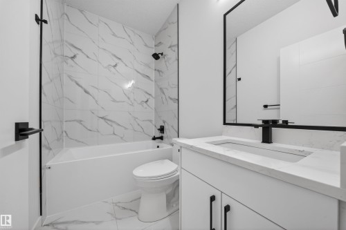 Contemporary bathroom featuring a white vanity with integrated sink, a large framed mirror, and a tub-shower combination with white-and-gray marbled tile surround - 3906 41 Avenue, Beaumont, AB - Indoor Photo Showing Bathroom