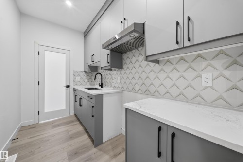 Modern kitchen featuring light wood-finish flooring, white countertops, and a striking geometric tile backsplash - 3906 41 Avenue, Beaumont, AB - Indoor Photo Showing Kitchen