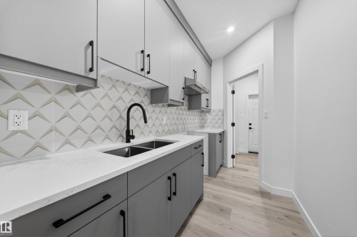 Modern kitchen featuring two-tone cabinetry, a dual basin undermount sink with a matte black faucet, and light-toned wood-finish flooring - 3906 41 Avenue, Beaumont, AB - Indoor Photo Showing Kitchen With Double Sink