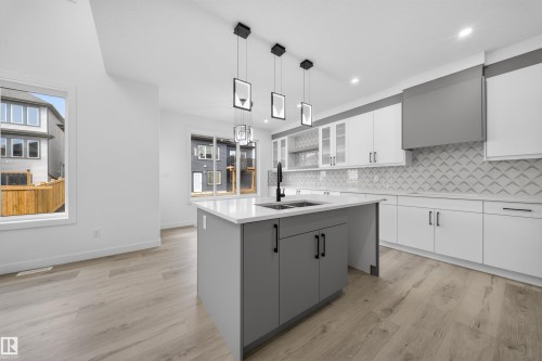 Modern kitchen featuring an expansive center island with an undermount double sink, white quartz countertops, and matte black hardware - 3906 41 Avenue, Beaumont, AB - Indoor Photo Showing Kitchen With Double Sink