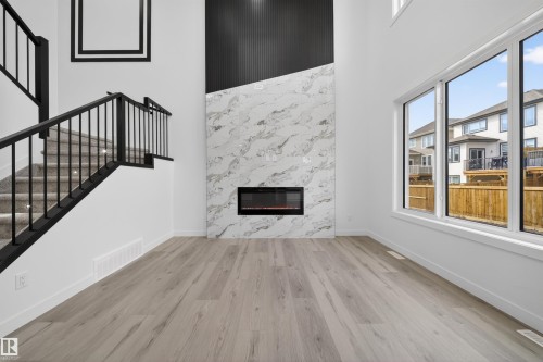 Spacious living area featuring a contemporary fireplace with a marble-finish surround, light wood-finish flooring, and large windows - 3906 41 Avenue, Beaumont, AB - Indoor With Fireplace