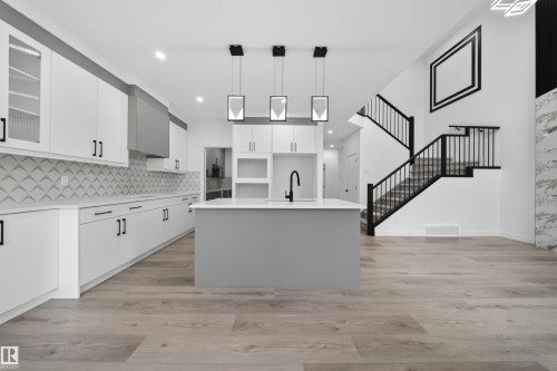 Open-concept kitchen featuring white cabinetry, a gray kitchen island with a black faucet, and a distinctive patterned tile backsplash - 3906 41 Avenue, Beaumont, AB - Indoor Photo Showing Kitchen