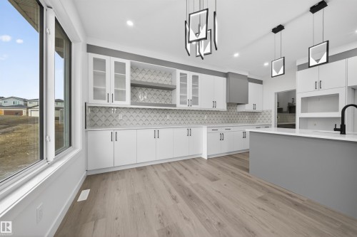 Spacious kitchen featuring an extended island with a white countertop, light wood-finish flooring, and a patterned tile backsplash - 3906 41 Avenue, Beaumont, AB - Indoor Photo Showing Kitchen With Upgraded Kitchen