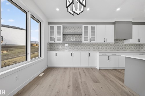 Spacious kitchen featuring white cabinetry, a geometric tile backsplash, a gray range hood, wood-finish flooring, and ample natural light from large windows - 3906 41 Avenue, Beaumont, AB - Indoor Photo Showing Kitchen