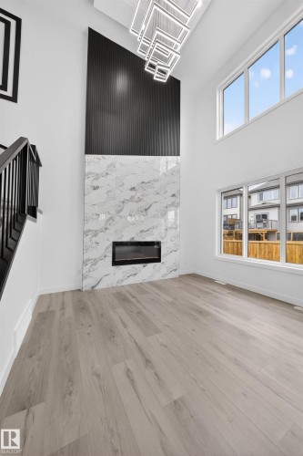 Vaulted ceiling living space featuring an electric fireplace with a marble-look surround, a fluted accent wall, and a multi-tiered contemporary chandelier - 3906 41 Avenue, Beaumont, AB - Indoor With Fireplace