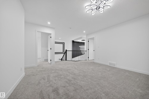 Expansive carpeted area featuring a modern ceiling light fixture, white walls, and recessed lighting, with a black metal railing - 3906 41 Avenue, Beaumont, AB - Indoor Photo Showing Other Room