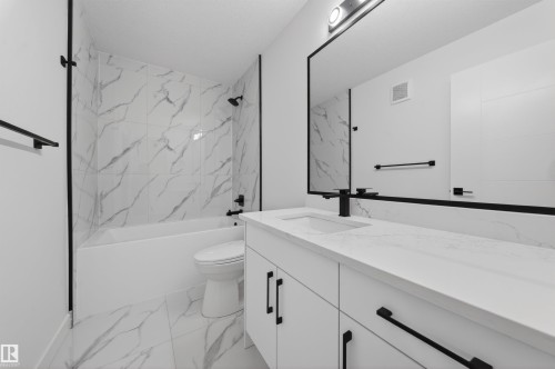 Bathroom featuring a white vanity with an integrated sink, black hardware, an expansive framed mirror, and a white bathtub with marble-look tile surround and black fixtures - 3906 41 Avenue, Beaumont, AB - Indoor Photo Showing Bathroom