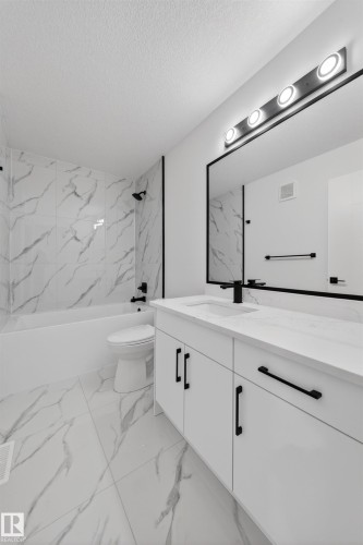Modern bathroom featuring a white vanity with black hardware, a black-framed mirror, and a four-bulb vanity light - 3906 41 Avenue, Beaumont, AB - Indoor Photo Showing Bathroom
