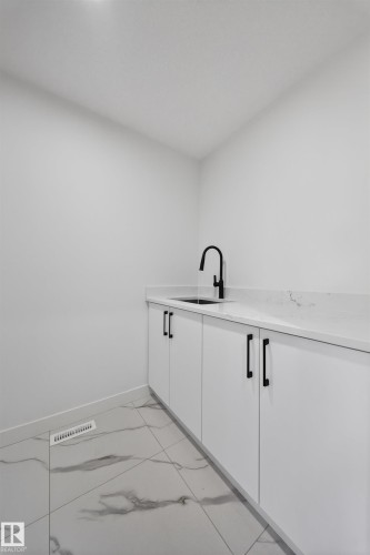 Utility area featuring marble-look tile flooring and white base cabinets with black hardware - 3906 41 Avenue, Beaumont, AB - Indoor