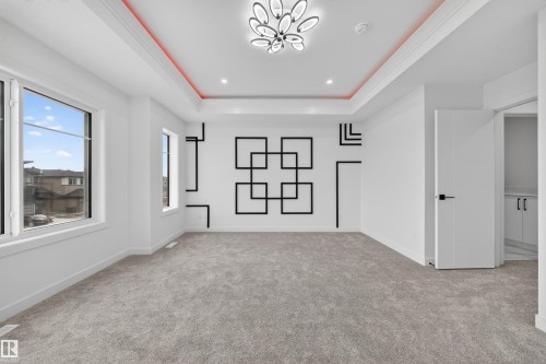 Spacious room featuring broadloom carpet, multiple windows, a decorative accent wall, a tray ceiling with integrated lighting, and a modern light fixture - 3906 41 Avenue, Beaumont, AB - Indoor Photo Showing Other Room