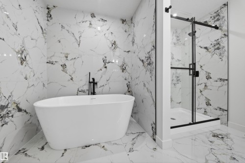 Freestanding soaking tub with a floor-mounted matte black faucet, surrounded by large format marble-look tile flooring and wall finishes - 3906 41 Avenue, Beaumont, AB - Indoor Photo Showing Bathroom