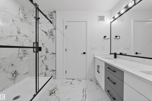Contemporary bathroom featuring a spacious walk-in shower with black-framed glass enclosure, marble-look wall and floor tile, and a double vanity with stone countertops - 3906 41 Avenue, Beaumont, AB - Indoor