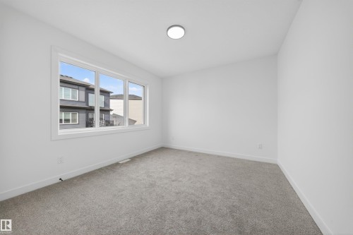 Bright room featuring a large triple-pane window, neutral gray carpet, white walls, and a flush-mount ceiling light fixture - 3906 41 Avenue, Beaumont, AB - Indoor Photo Showing Other Room