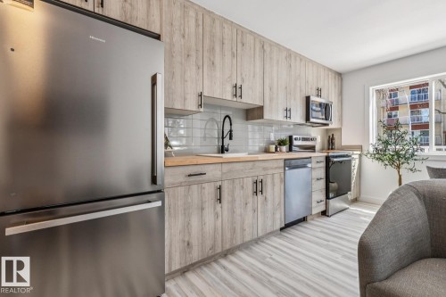 Modern kitchen featuring wood-finish cabinetry, stainless steel appliances, light wood-finish countertops, subway tile backsplash, and a large window - 10726 107 Street, Edmonton, AB - Indoor Photo Showing Kitchen With Stainless Steel Kitchen