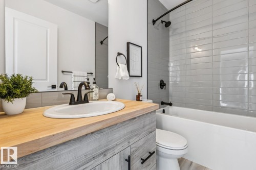 Bathroom featuring a wood-finish vanity with an integrated white sink and dark bronze faucet, white bathtub with grey subway tile surround, and coordinating dark bronze shower fixtures - 10726 107 Street, Edmonton, AB - Indoor Photo Showing Bathroom