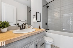 Bathroom featuring a wood-finish vanity with an integrated white sink and dark bronze faucet, white bathtub with grey subway tile surround, and coordinating dark bronze shower fixtures - 