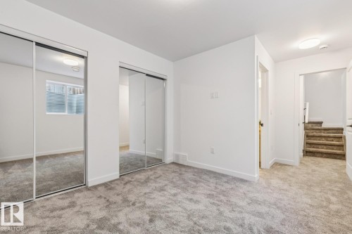 Bedroom featuring two mirrored sliding door closets, neutral gray carpet, white walls, and a window with horizontal blinds - 10726 107 Street, Edmonton, AB - Indoor Photo Showing Other Room