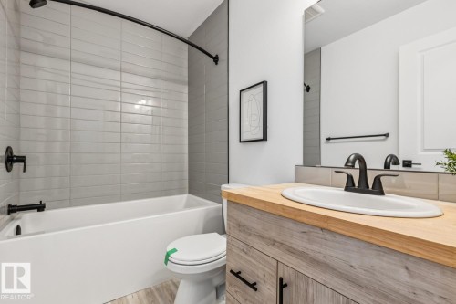 Modern bathroom featuring a white bathtub and toilet, light gray subway tile surround, matte black fixtures, and a vanity with a light wood-finish countertop and sink - 10726 107 Street, Edmonton, AB - Indoor Photo Showing Bathroom