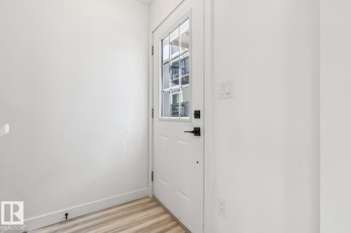 Entryway featuring a white paneled door with multiple glass panes and matte black hardware, light wood-finish flooring, and crisp white walls - 10726 107 Street, Edmonton, AB - Indoor Photo Showing Other Room