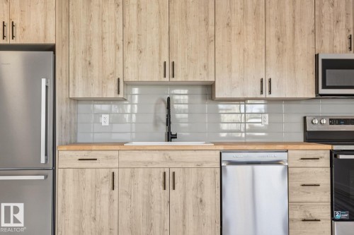 Kitchen featuring wood-finish cabinetry, light wood countertops, a light gray subway tile backsplash, and stainless steel appliances including a refrigerator, dishwasher, and range - 10726 107 Street, Edmonton, AB - Indoor Photo Showing Kitchen With Stainless Steel Kitchen