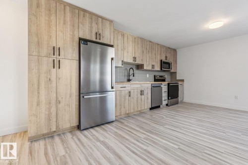 Open-concept kitchen featuring wood-look cabinetry, stainless steel appliances, a subway tile backsplash, and wood-finish flooring - 10726 107 Street, Edmonton, AB - Indoor Photo Showing Kitchen With Stainless Steel Kitchen