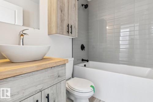 Bathroom featuring a white vessel sink, wood-finish vanity with matte black hardware, and a white bathtub with subway tile surround - 10726 107 Street, Edmonton, AB - Indoor Photo Showing Bathroom