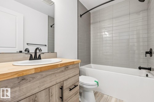 Bathroom featuring a wood-finish vanity with an undermount sink, matte black faucet, and a large mirror - 10726 107 Street, Edmonton, AB - Indoor Photo Showing Bathroom