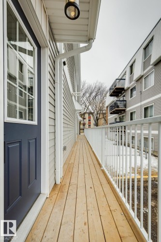 Exterior entryway featuring a dark blue door with a large window, light gray siding, a wood-plank walkway, white railings, and an overhead light fixture - 10726 107 Street, Edmonton, AB - Outdoor With Exterior