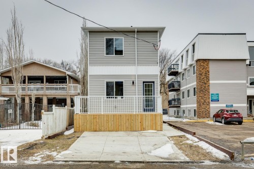 Contemporary two-story residence featuring light gray siding with white trim, a front wood-finish deck with white railings, and an integrated concrete parking pad - 10726 107 Street, Edmonton, AB - Outdoor