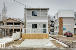 Contemporary two-story residence featuring light gray siding with white trim, a front wood-finish deck with white railings, and an integrated concrete parking pad - 