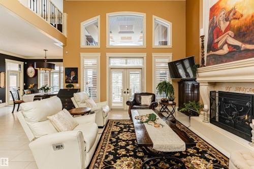 The living area features a large fireplace with an ornate mantel, towering windows with arch details, and a dark ornate area rug - 3048 Watson Landing, Edmonton, AB - Indoor Photo Showing Other Room With Fireplace