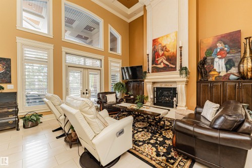 Living area featuring high ceilings, large windows with shutters, and a fireplace with a decorative mantel - 3048 Watson Landing, Edmonton, AB - Indoor Photo Showing Living Room With Fireplace