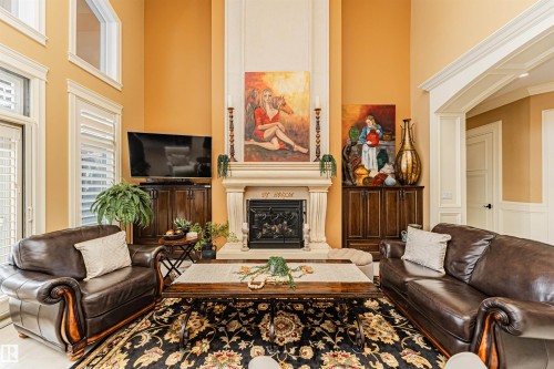 The spacious living area features high ceilings, large windows with white louvered shutters, and a prominent fireplace with an ornate mantel and hearth - 3048 Watson Landing, Edmonton, AB - Indoor Photo Showing Living Room With Fireplace
