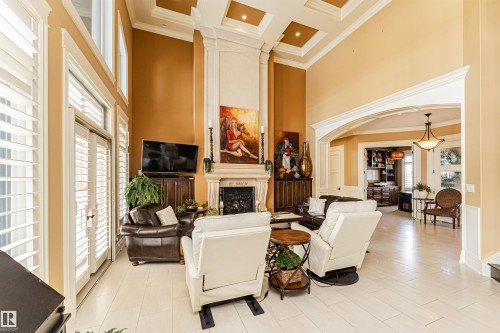 Living room featuring a tall fireplace with an ornate mantel, high ceilings with decorative trim, and light-colored flooring - 3048 Watson Landing, Edmonton, AB - Indoor With Fireplace