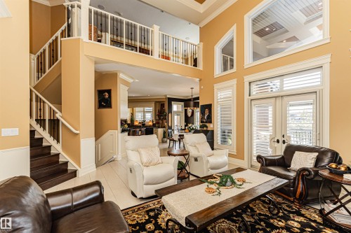 Grand living area featuring high ceilings, large windows with shutters, and a prominent staircase with a balcony overlooking the space - 3048 Watson Landing, Edmonton, AB - Indoor Photo Showing Living Room