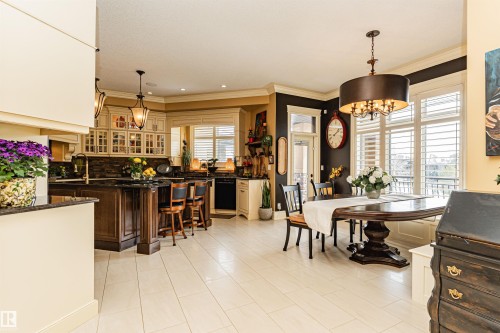 The open concept kitchen and dining areas feature light-colored tile flooring, a kitchen island with seating, dark wood cabinetry, and large windows with plantation shutters - 3048 Watson Landing, Edmonton, AB - Indoor Photo Showing Dining Room