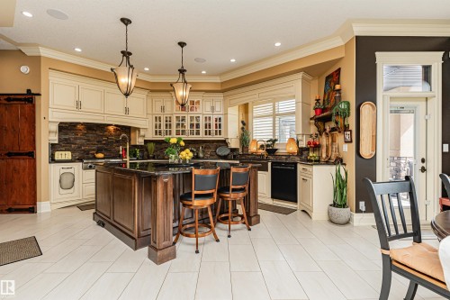 The kitchen features a large central island with a dark countertop and bar seating, complemented by cream-colored cabinetry and a dark stone-tiled backsplash - 3048 Watson Landing, Edmonton, AB - Indoor