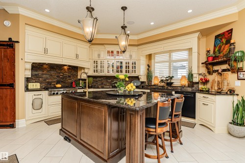 The kitchen features an island with a dark granite countertop, light-colored cabinetry, a stone tile backsplash, and a built-in range - 3048 Watson Landing, Edmonton, AB - Indoor Photo Showing Kitchen