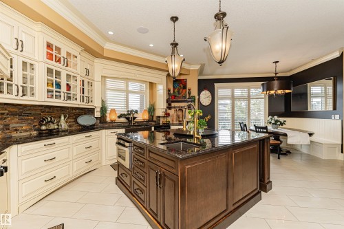The kitchen features a large island with a sink, white cabinetry, a stone backsplash, dark countertops, and a dining area with a built-in bench and large windows - 3048 Watson Landing, Edmonton, AB - Indoor Photo Showing Kitchen