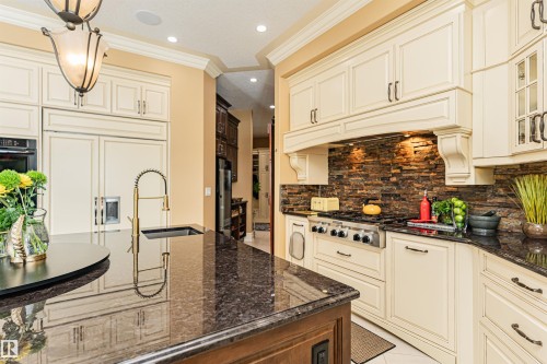 Well-appointed kitchen featuring cream-colored cabinetry, dark granite countertops, and a stone-tiled backsplash - 3048 Watson Landing, Edmonton, AB - Indoor Photo Showing Kitchen With Upgraded Kitchen