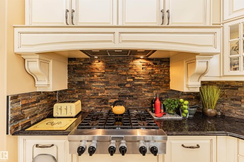 The kitchen features a stainless steel range with a ventilation hood, a dark granite countertop, and a stacked stone backsplash - 3048 Watson Landing, Edmonton, AB - Indoor Photo Showing Kitchen