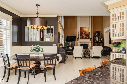 This interior offers an open layout featuring a dining area with a chandelier, a living area with a fireplace, and light-colored flooring - 3048 Watson Landing, Edmonton, AB - Indoor Photo Showing Dining Room