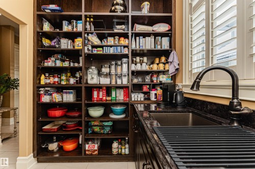 This well-appointed pantry features extensive dark wood shelving, a built-in counter with a sink, and dark granite countertops. formally known as a butler pantry. - 3048 Watson Landing, Edmonton, AB - Indoor